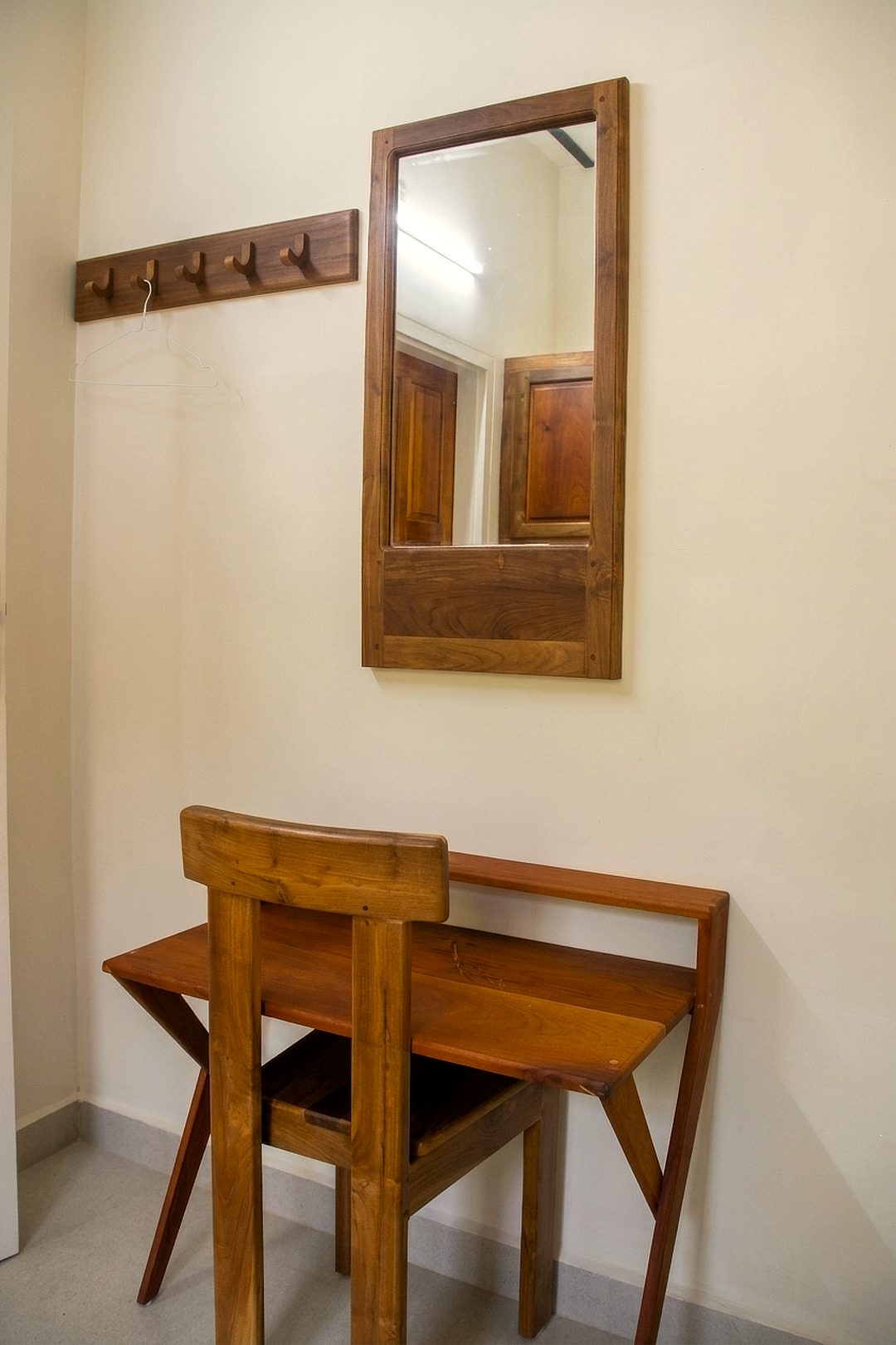 Wooden writing desk and chair below a wall mirror